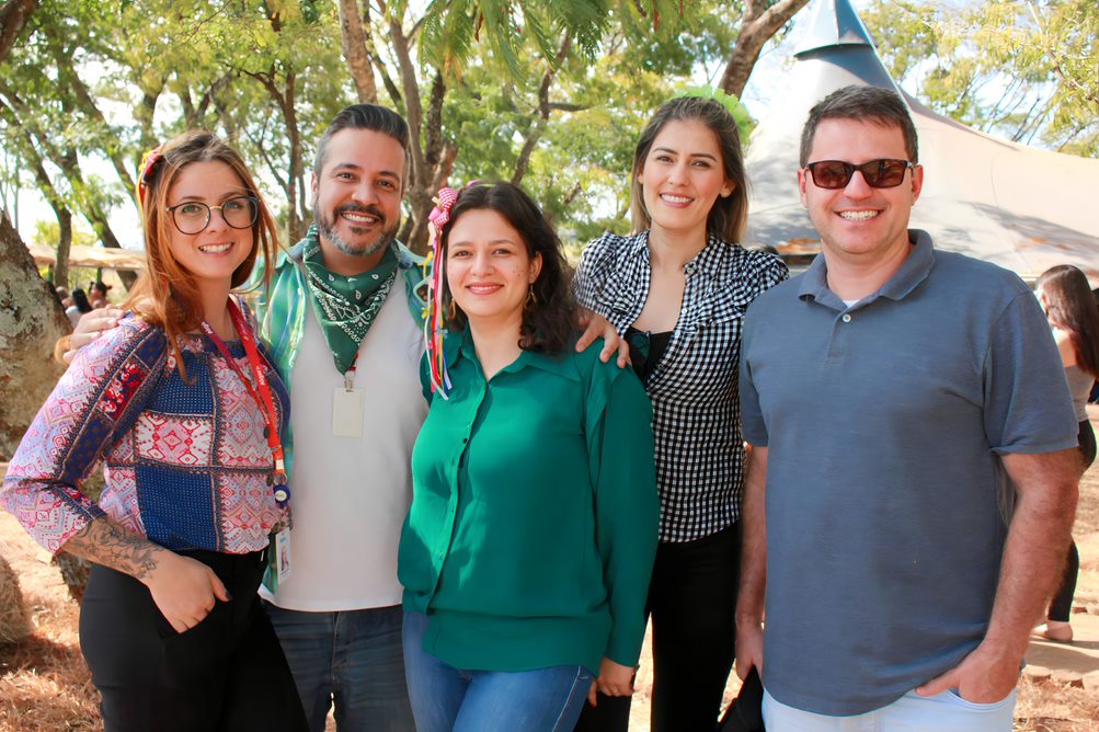 Na imagem de capa temos cinco pessoas em um local aberto com arvores ao fundo. Da esquerda para direita temos: uma mulher branca, ruiva, de óculos, com calça preta e camisa azul e vermelha, um homem branco com calça jeans, camisa branca e um lenço verde no pescoço, uma mulher branca de cabelos escuros de calça jeans e camisa verde, mulher alta branca e loira usando calça preta e uma camisa xadrez em preto e branco e um homem branco de óculos de sol com calça jeans e camisa polo cinza escura.