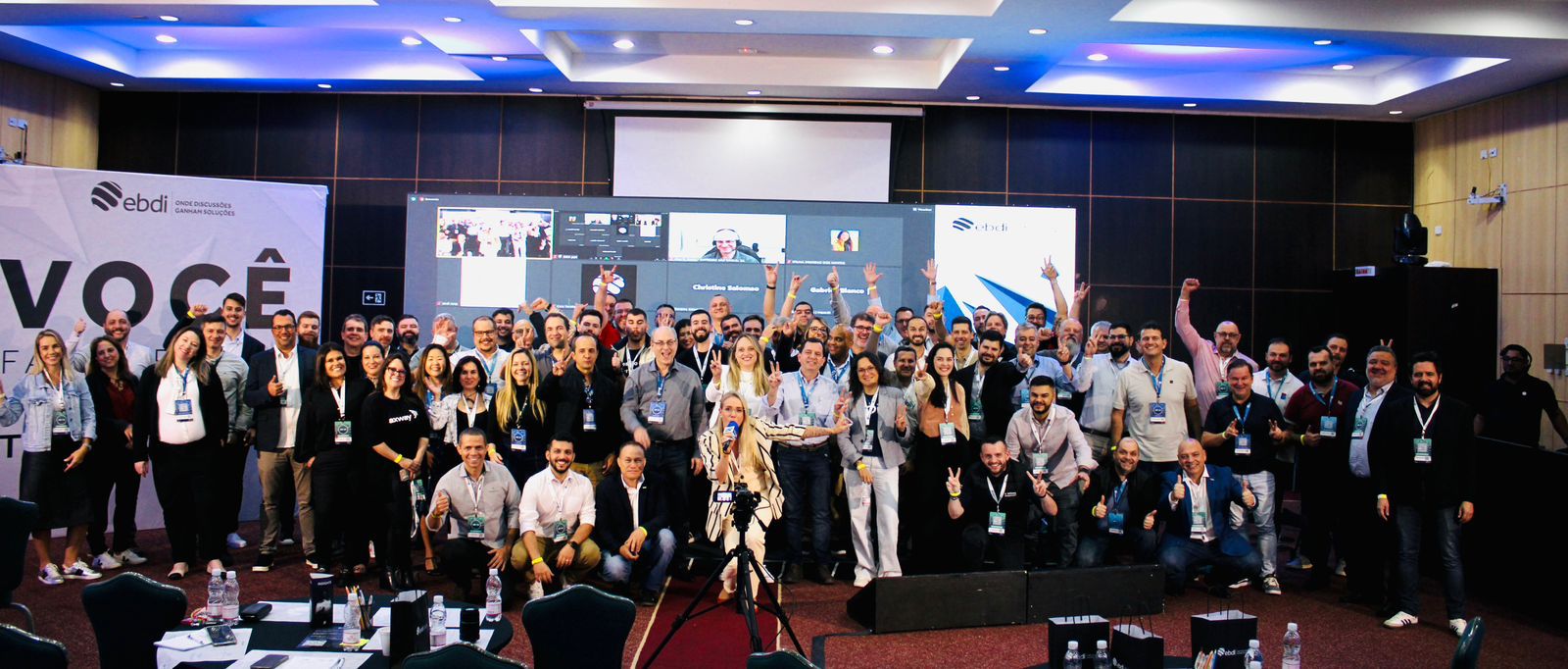 Na imagem vemos vários executivos, alguns de pé outros agachados posando para foto sorrindo em uma sala de conferencias.